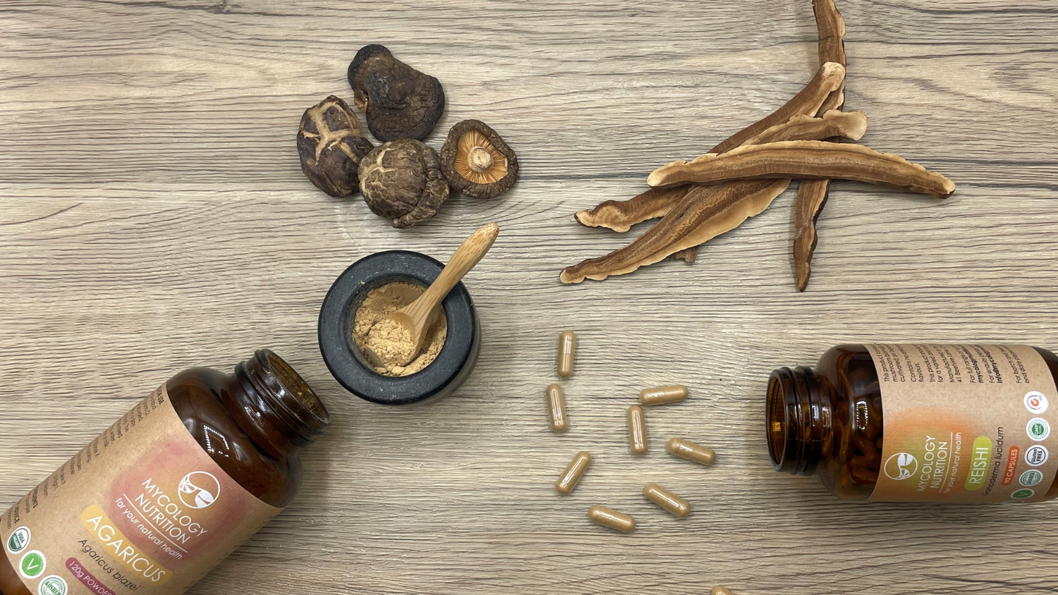 Functional mushroom supplements with Reishi and Agaricus bottles as well as dried mushrooms on a wooden surface.