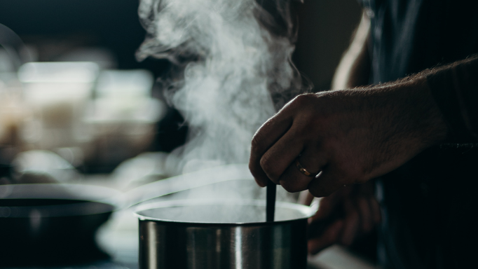 A close-up of a person's hand stirring a steaming pot.
