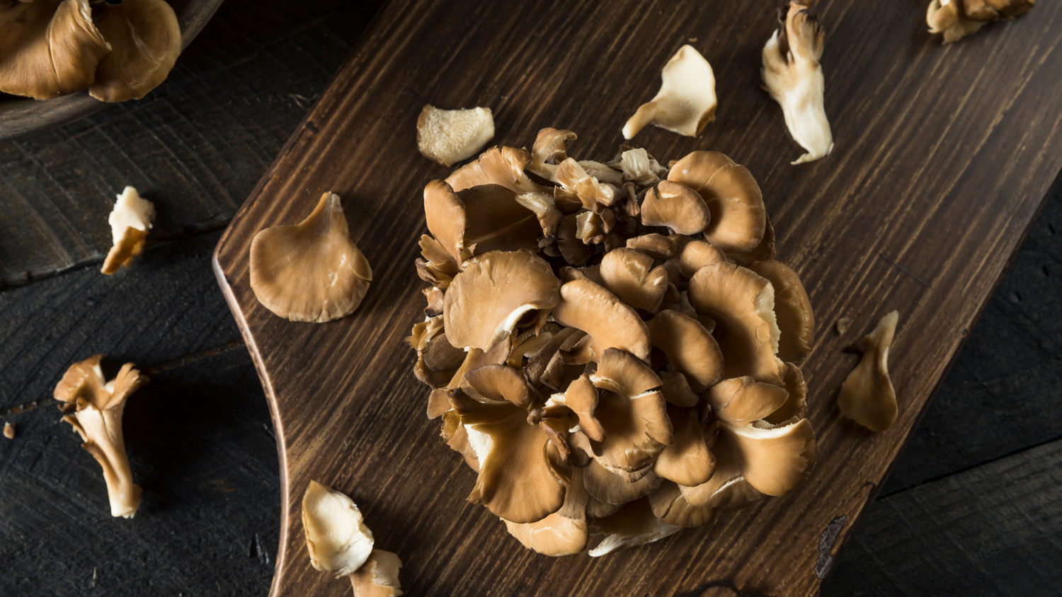 Fresh Maitake mushroom on a wooden board with scattered mushroom pieces around it.