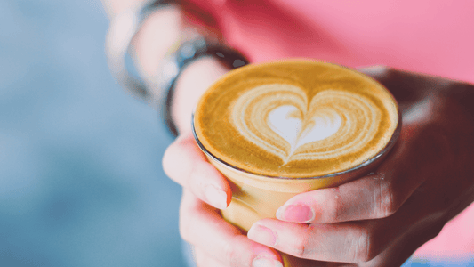 A person holding a cup of coffee with heart-shaped latte art on the surface.